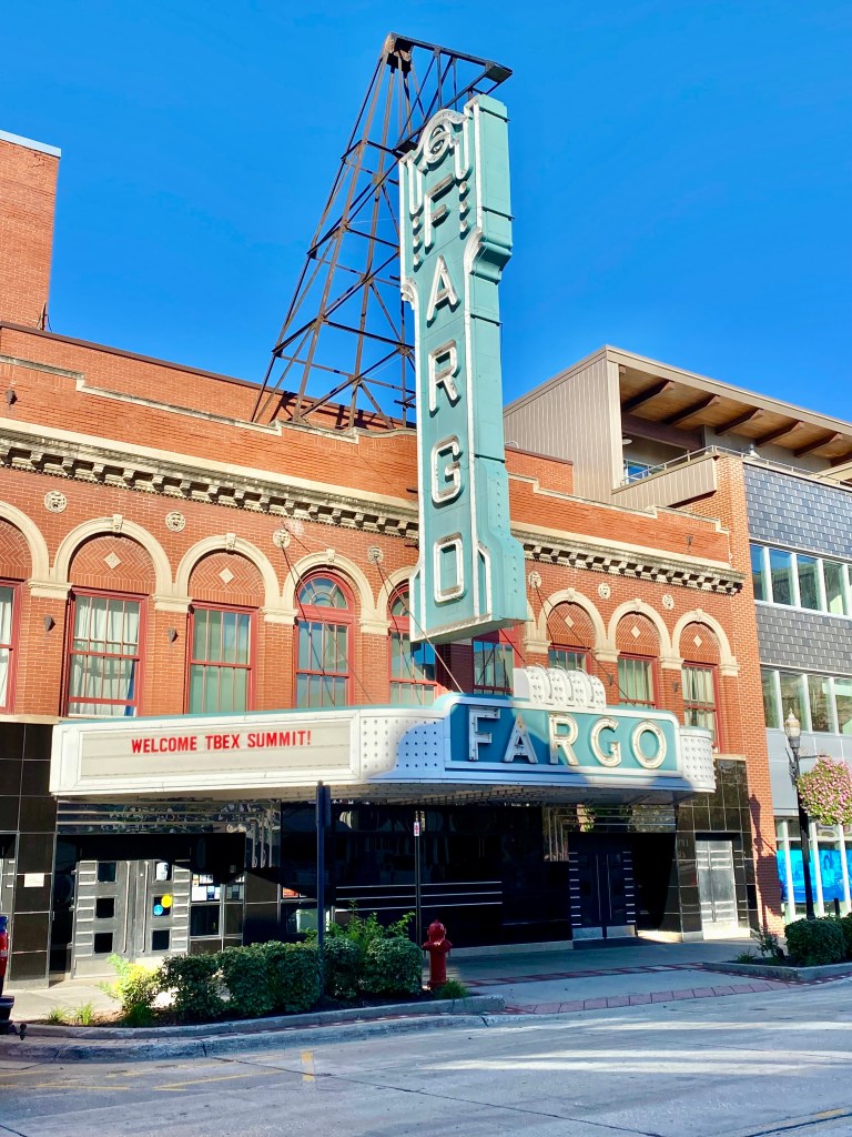 Exterior view of the Fargo Theater featuring a large marquee reading 'WELCOME TBEX SUMMIT!' against a clear blue sky.